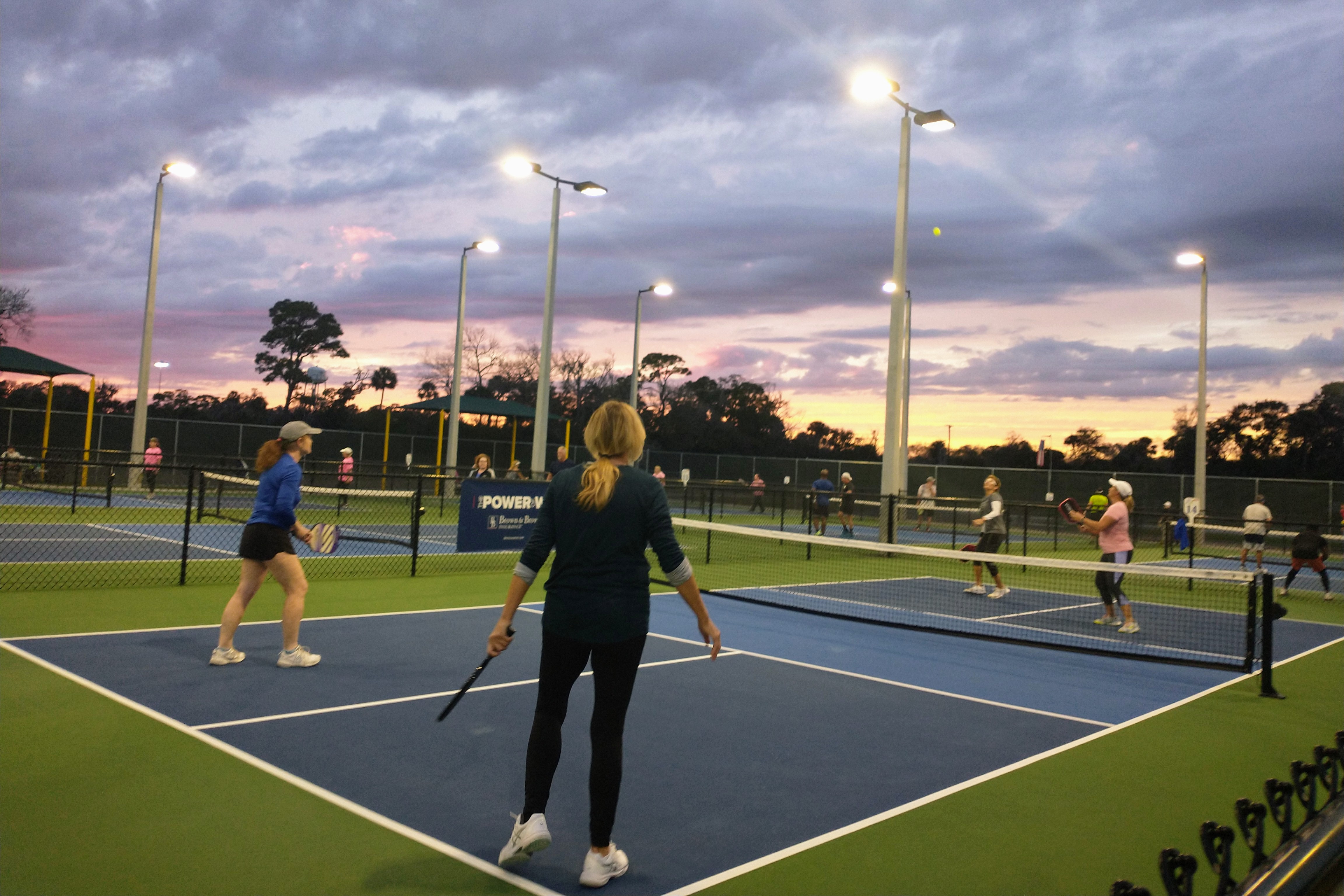 Players competing at sunset under illuminated court lights